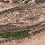 Vista aérea de um leito de rio seco, com pedras, solo exposto e vegetação esparsa.