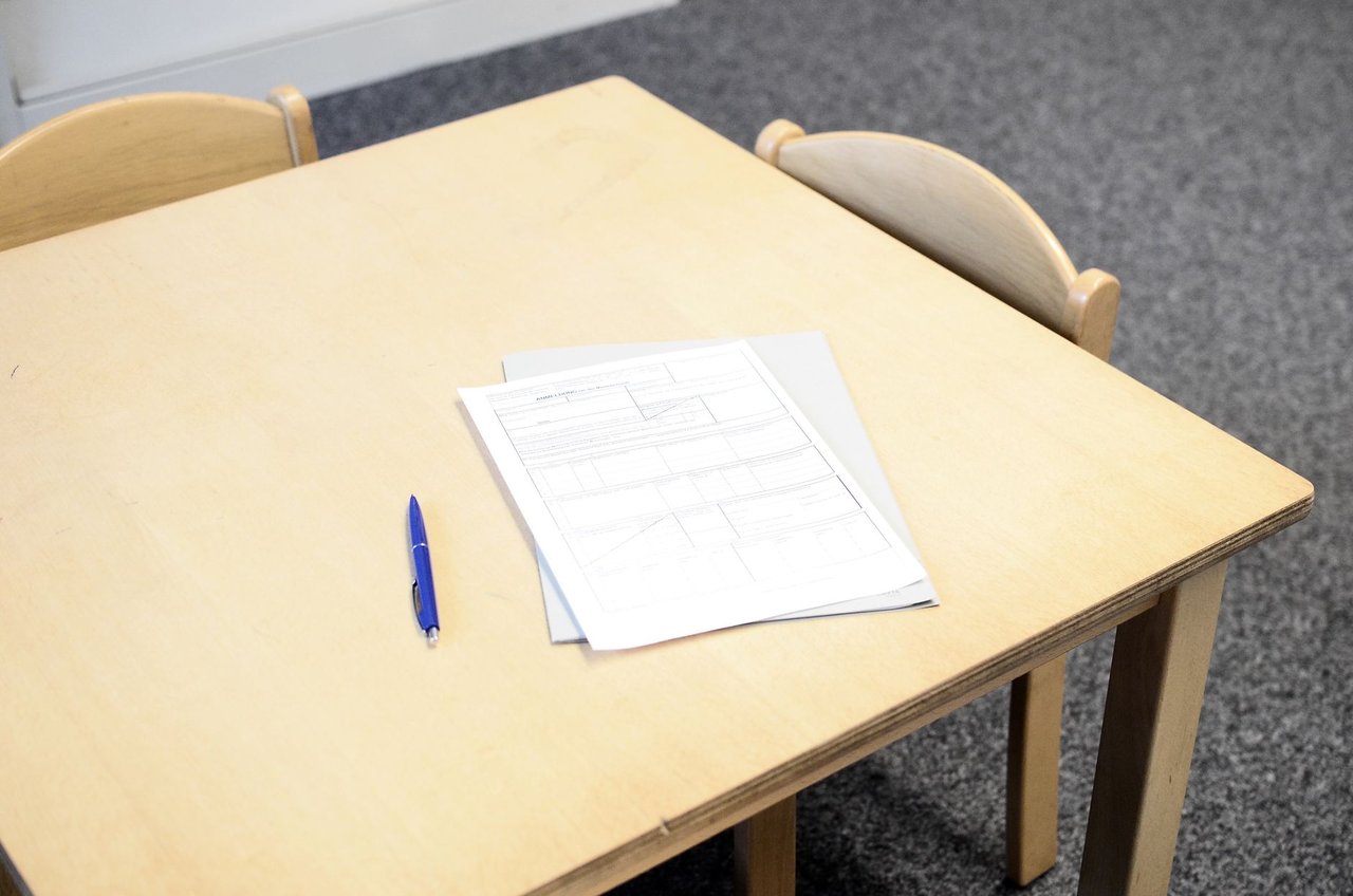 Documentos e uma caneta organizados sobre uma mesa próxima a cadeiras em uma sala clara.