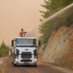 Bombeiros equipados usam um caminhão com canhão de água para combater um incêndio florestal.