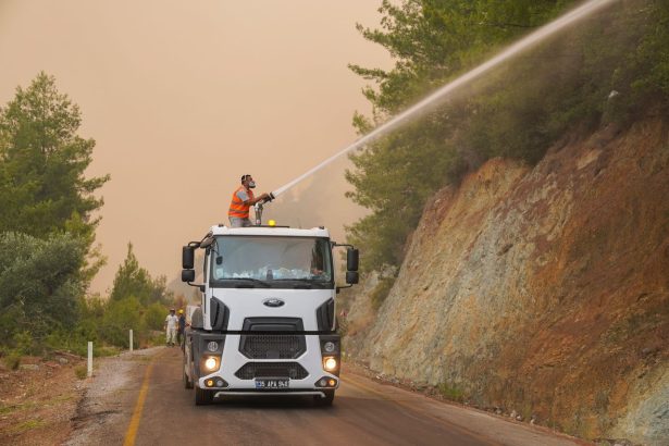Bombeiros equipados usam um caminhão com canhão de água para combater um incêndio florestal.