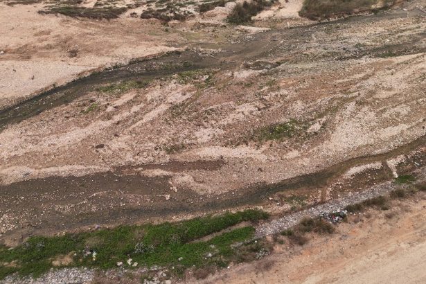 Vista aérea de um leito de rio seco, com pedras, solo exposto e vegetação esparsa.