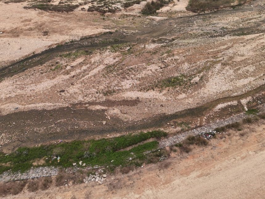 Vista aérea de um leito de rio seco, com pedras, solo exposto e vegetação esparsa.
