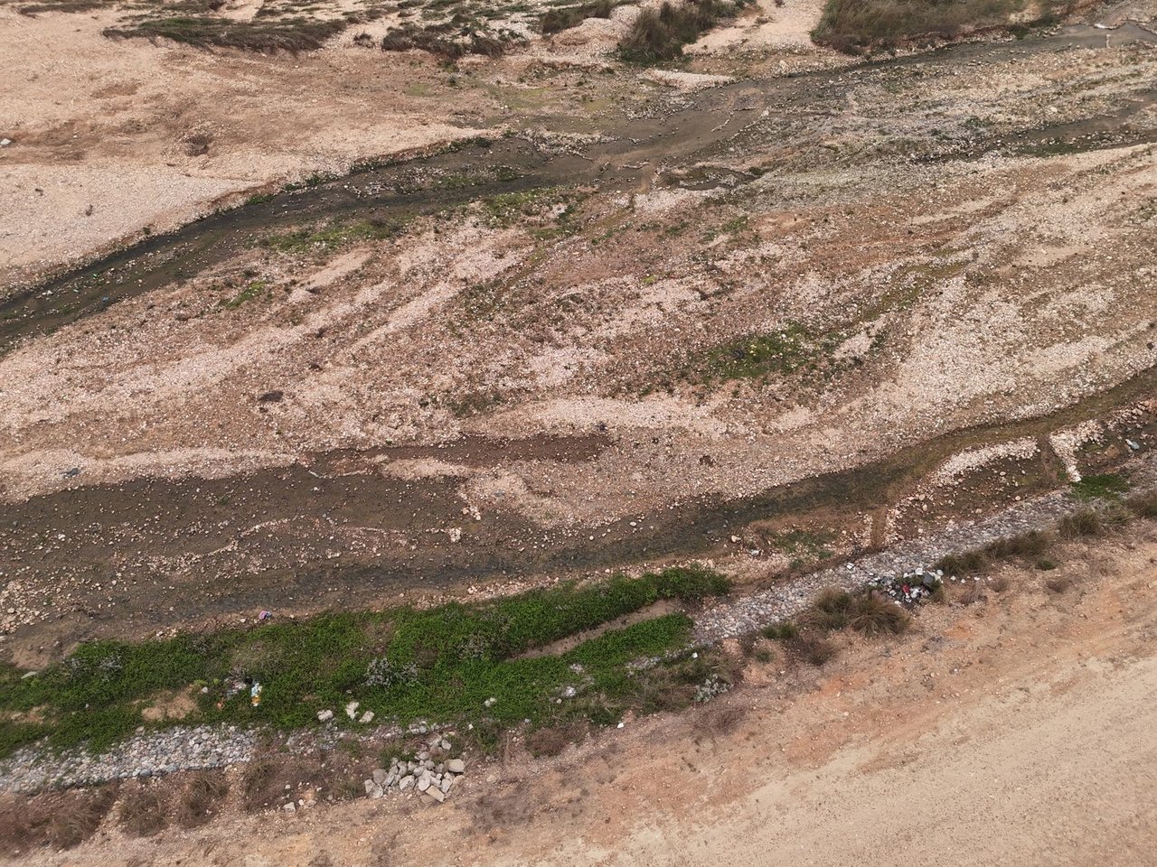 Vista aérea de um leito de rio seco, com pedras, solo exposto e vegetação esparsa.